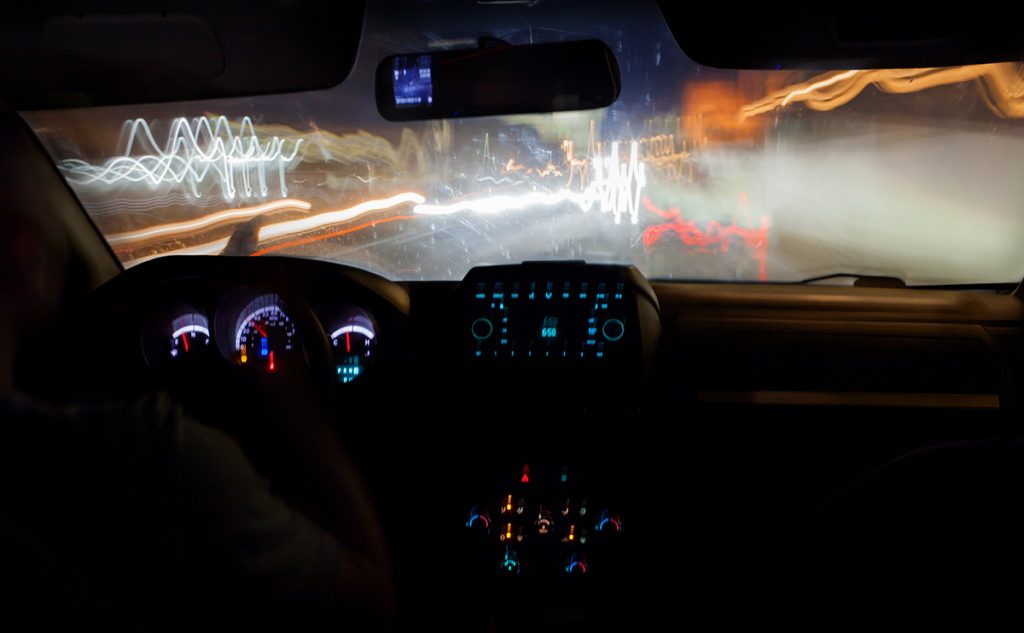 Driving a car in the city at night. Traveling on high speed, road lights defocused. View from inside with luminous dashboard